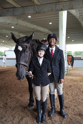 a young boy and girl in English riding attire next to a black horse with a white patch on the face